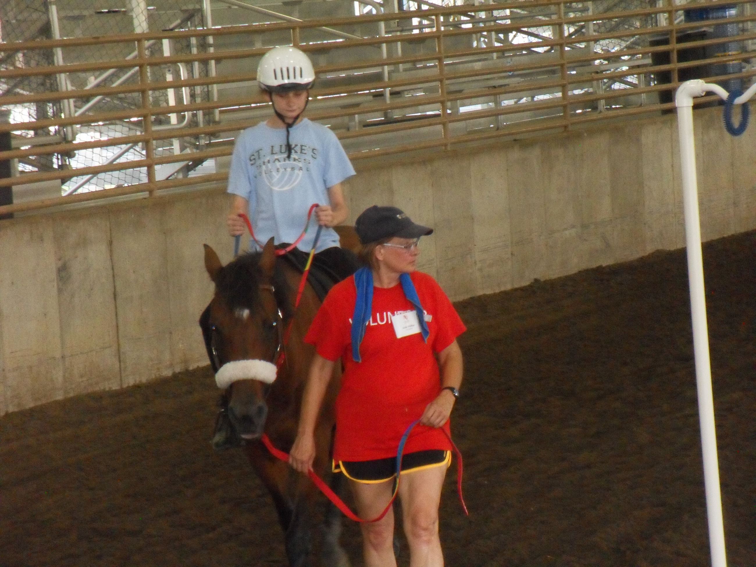 Woman guiding a horse with a kid on it around the arena