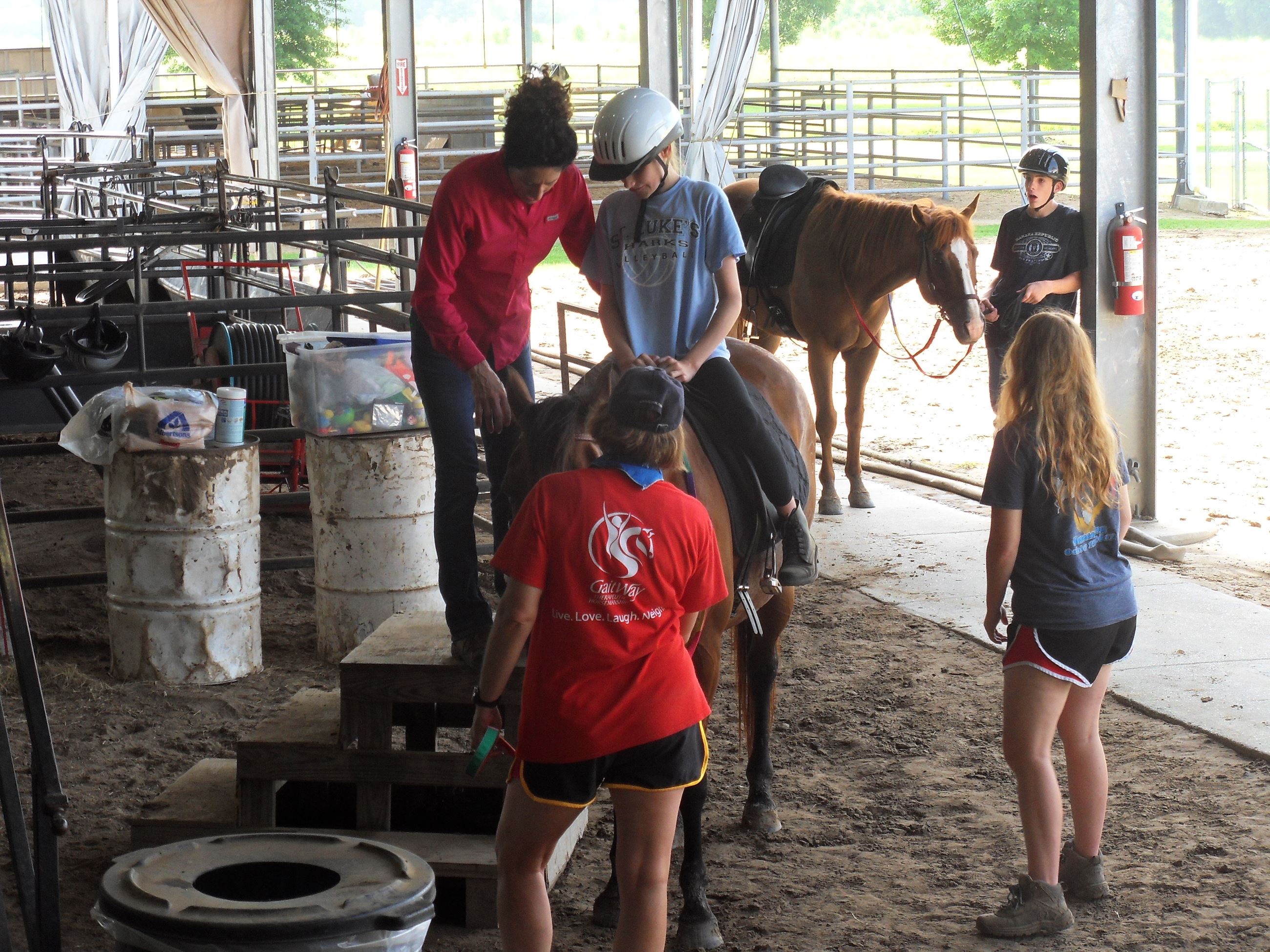 Woman helping kid get onto a horse